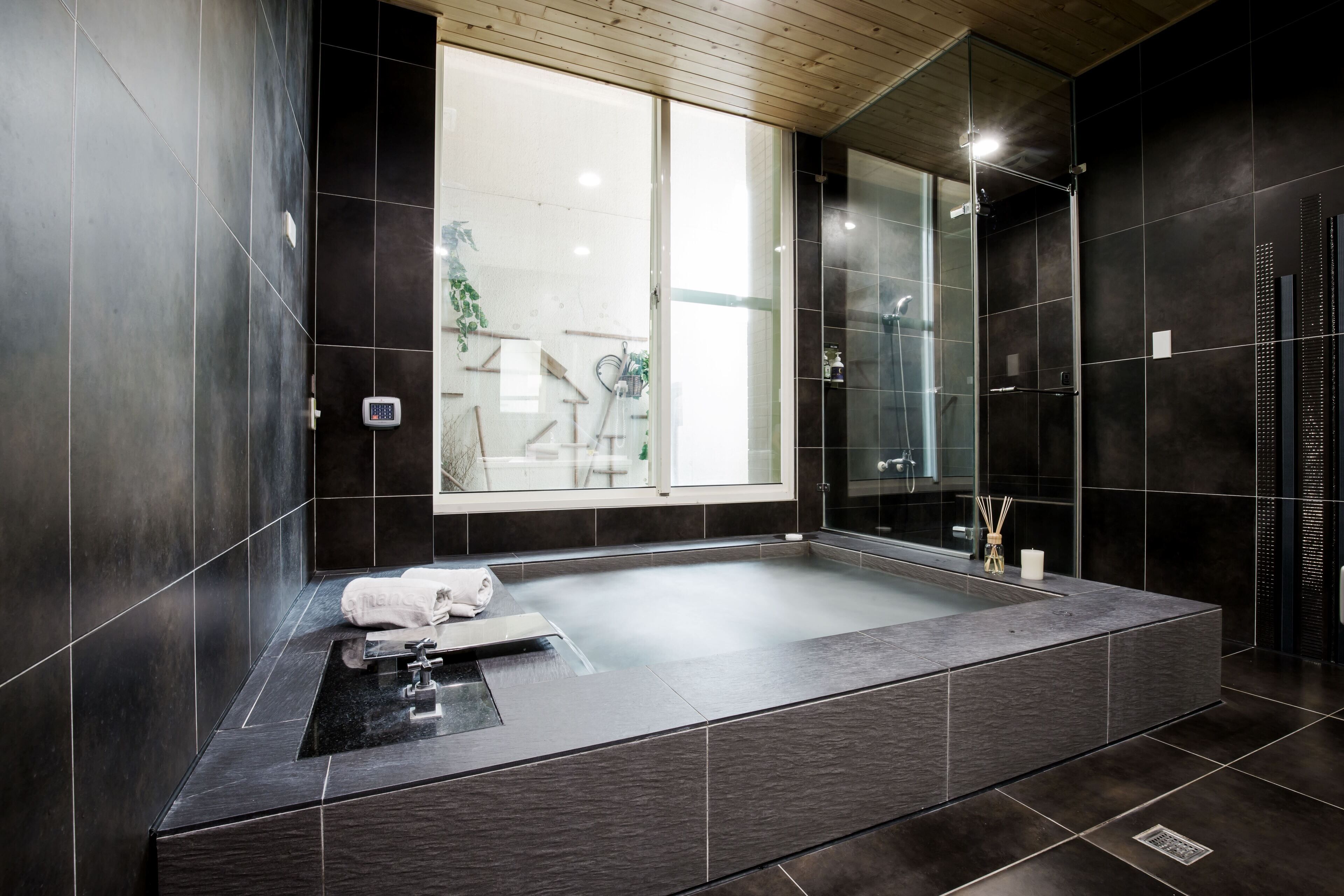 A modern bathroom with a large bathtub, a glass shower enclosure, and a view of a balcony.