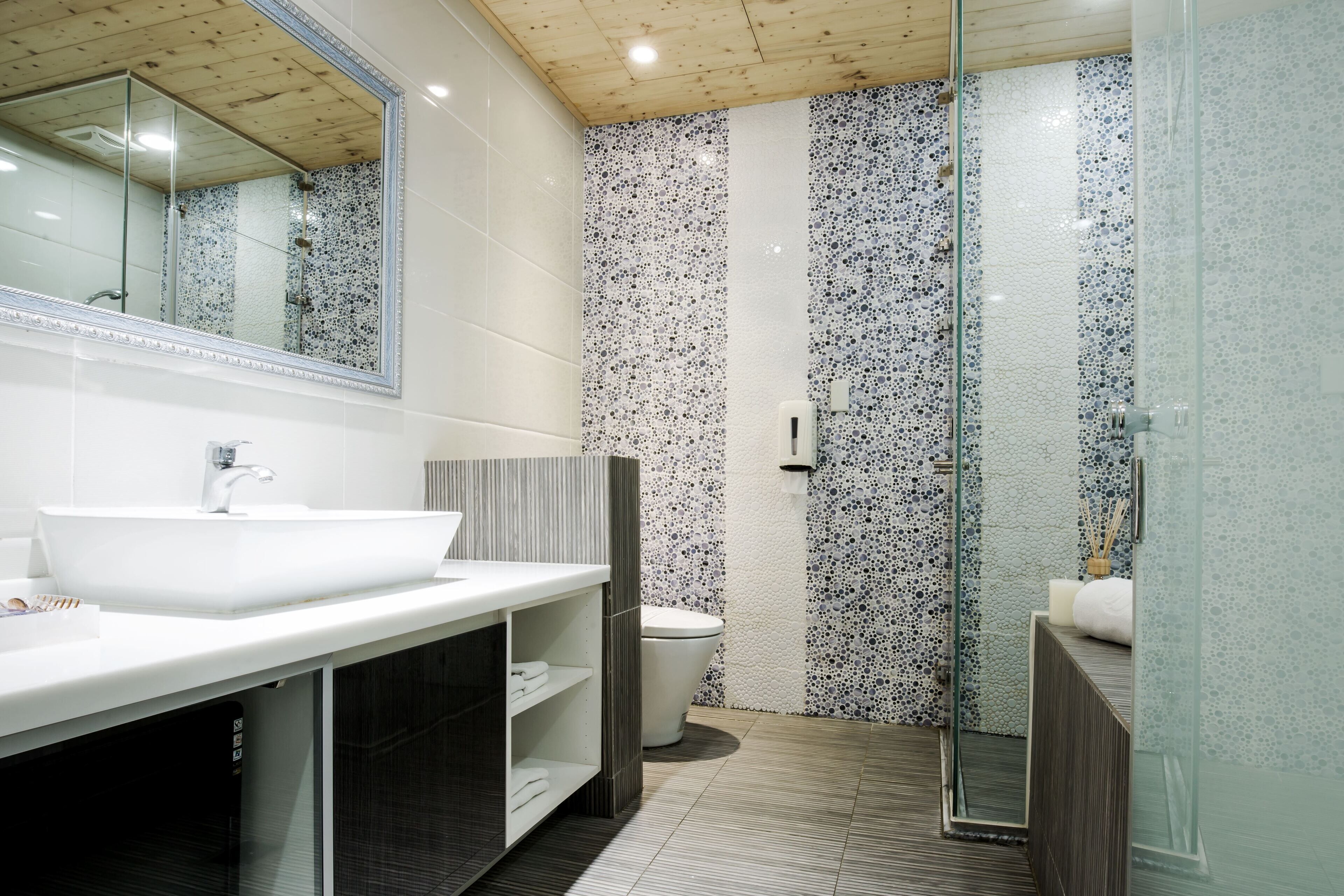 Un baño moderno con un lavamanos grande de color blanco, cabina de ducha de vidrio y pared de ducha con azulejos.