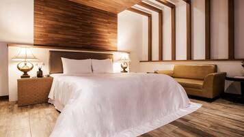 A modern hotel room with a wooden ceiling, a large bed with white linens, two bedside lamps, a brown armchair, and a small side table.
