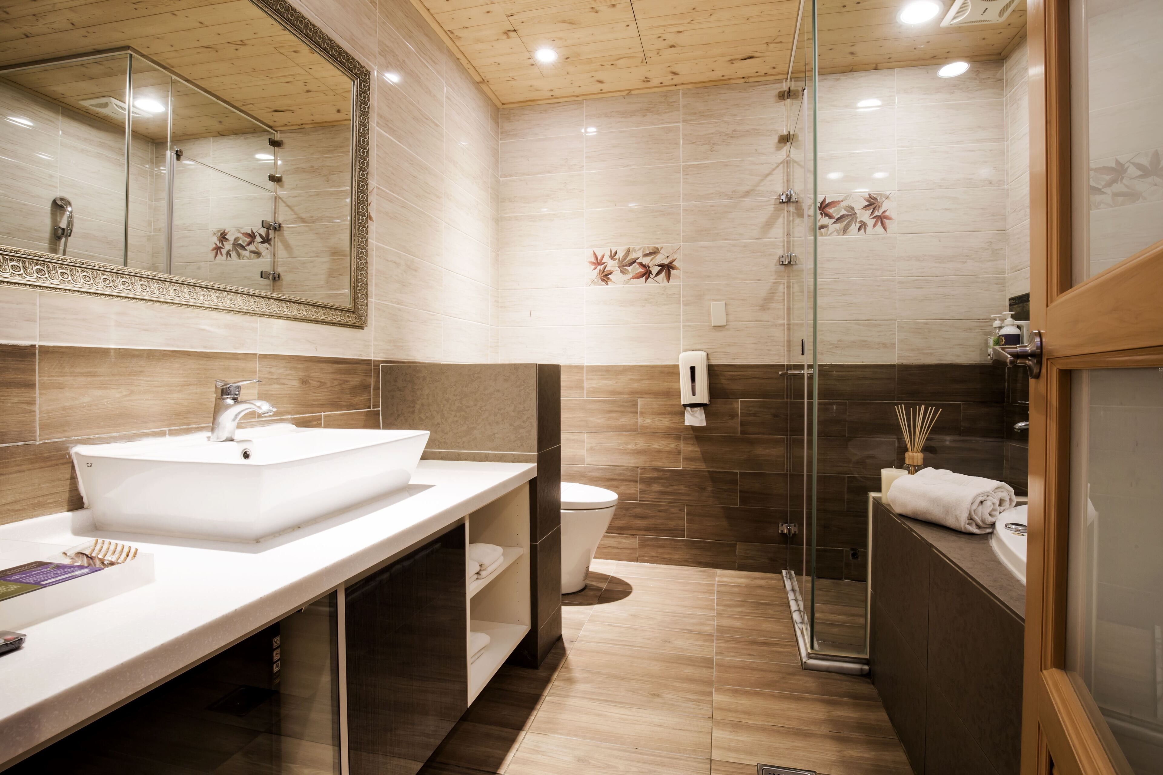 A modern bathroom with a large mirror, a white sink, a glass shower enclosure, and a toilet.