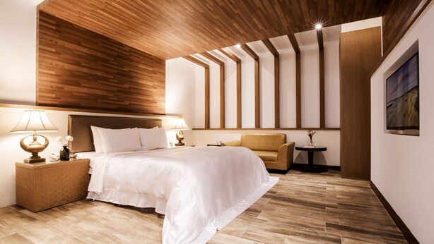 Een moderne hotelkamer met een houten plafond, een groot bed, een bank, een klein tafeltje en een tv aan de muur.