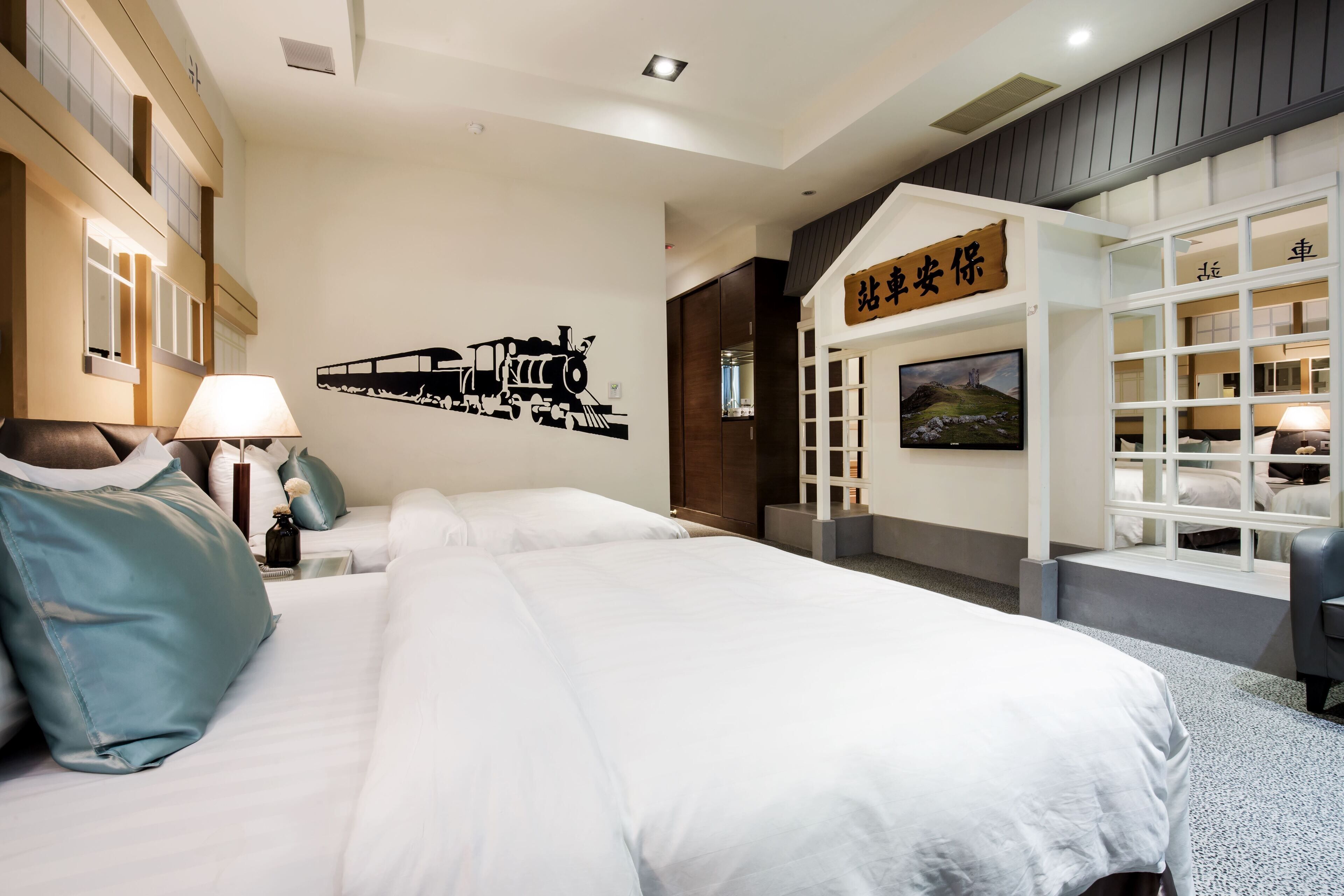 A hotel room with a large bed, a wall-mounted artwork of a train, a wooden sign with Chinese characters, and a window with a view of a landscape.