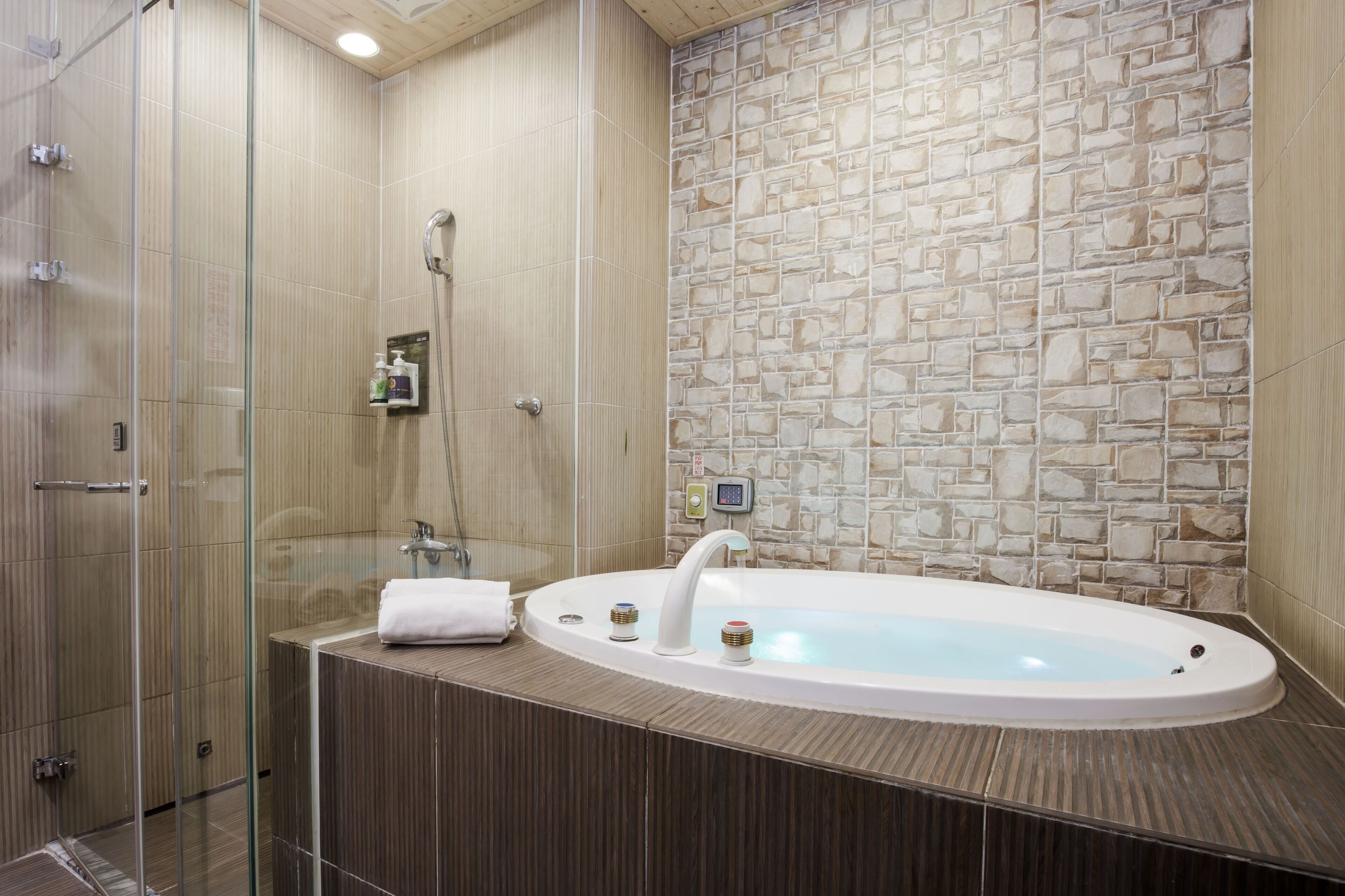 A modern bathroom with a stone wall, a glass shower enclosure, and a freestanding bathtub.