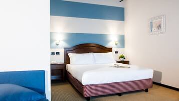 Una habitación de hotel con una cama grande, una mesita de noche, una silla azul y una pared con estampado azul y blanco a rayas.