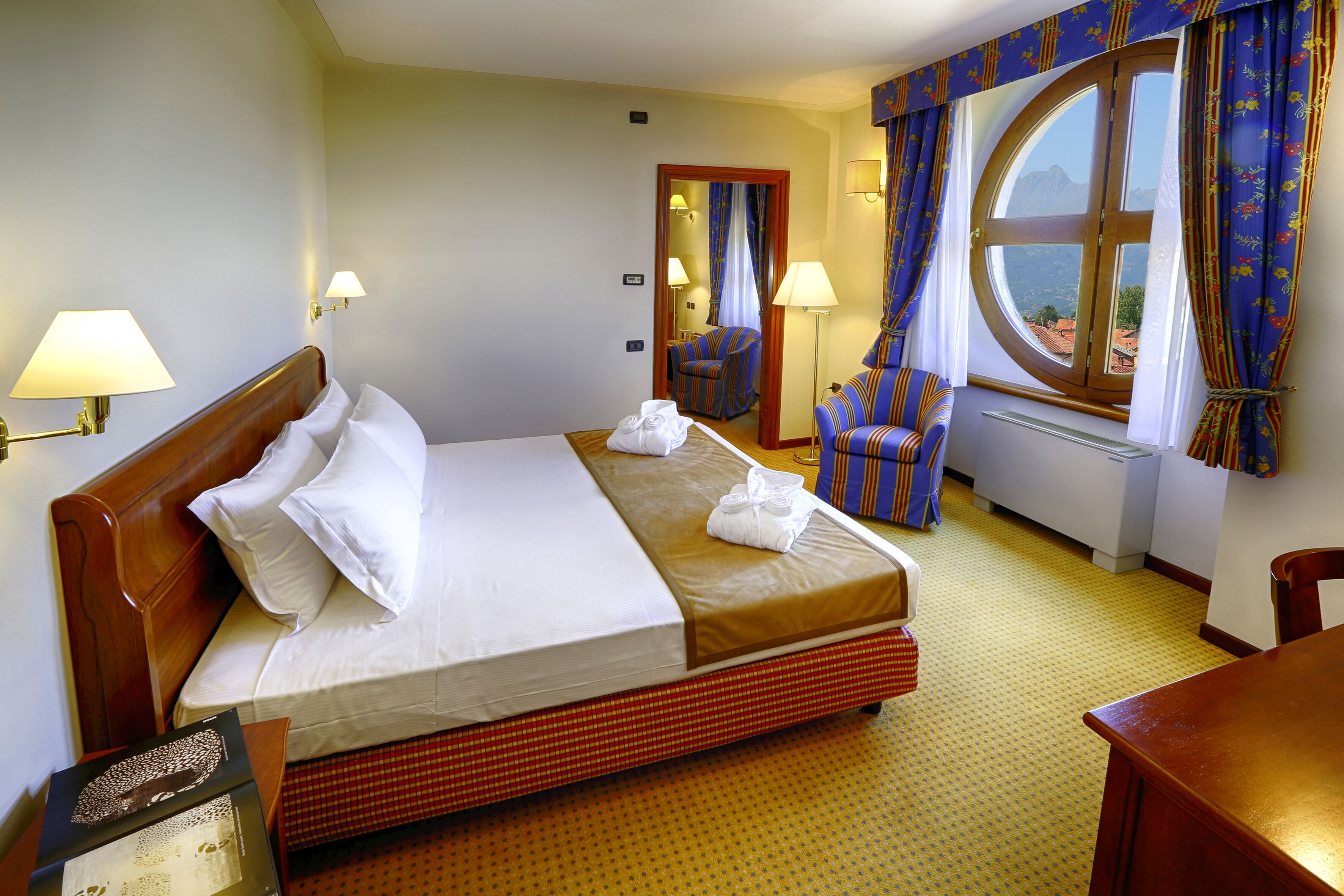 A hotel room with a large bed, a chair, a desk, and a window with curtains.