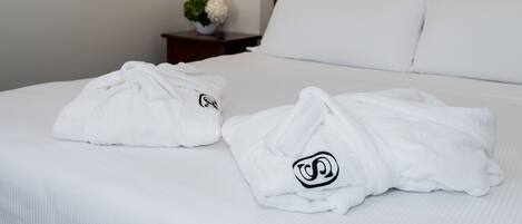 Una cama bien hecha con sábanas blancas y dos batas de baño blancas con un logotipo.