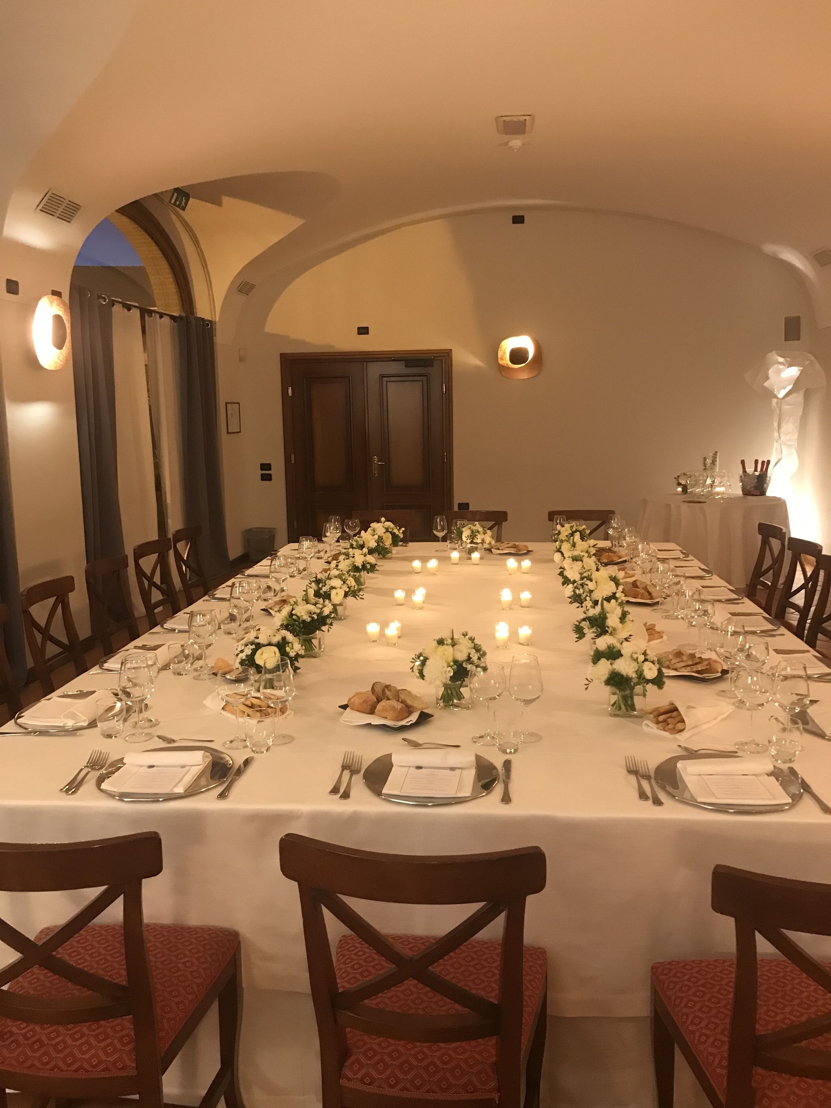 A long dining table set for a formal meal with candles, floral centerpieces, and neatly arranged tableware.