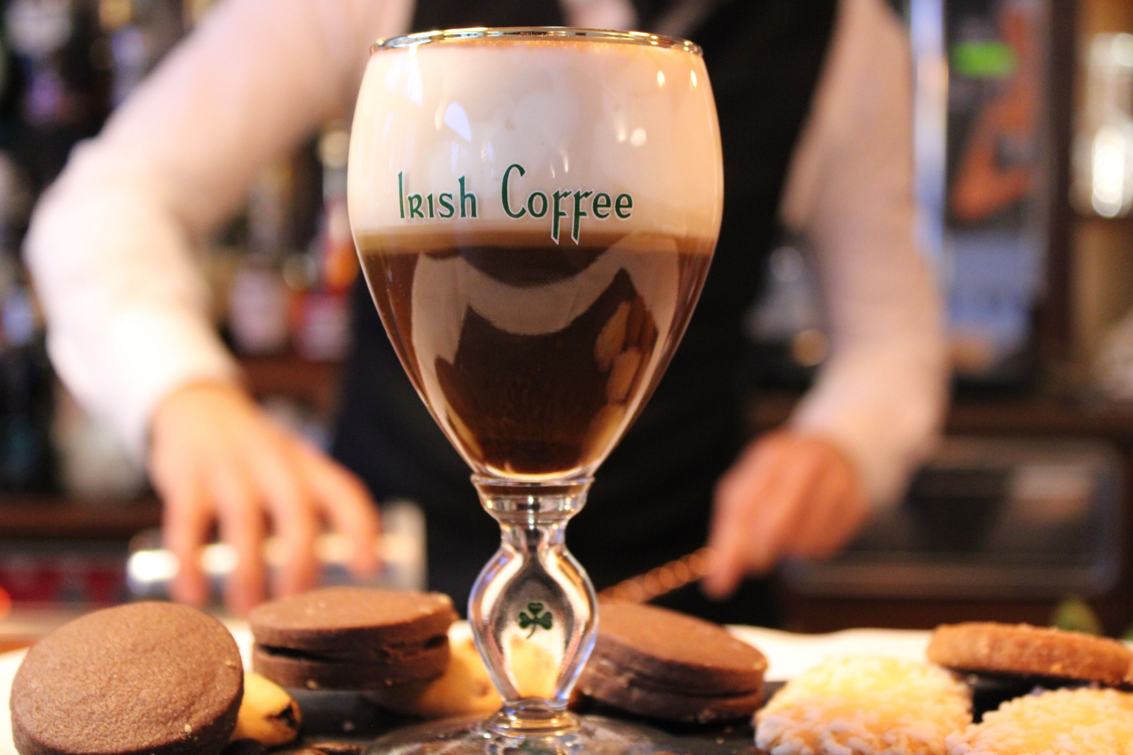 A glass of coffee with "Irish Coffee" written on it, placed on a table with cookies.