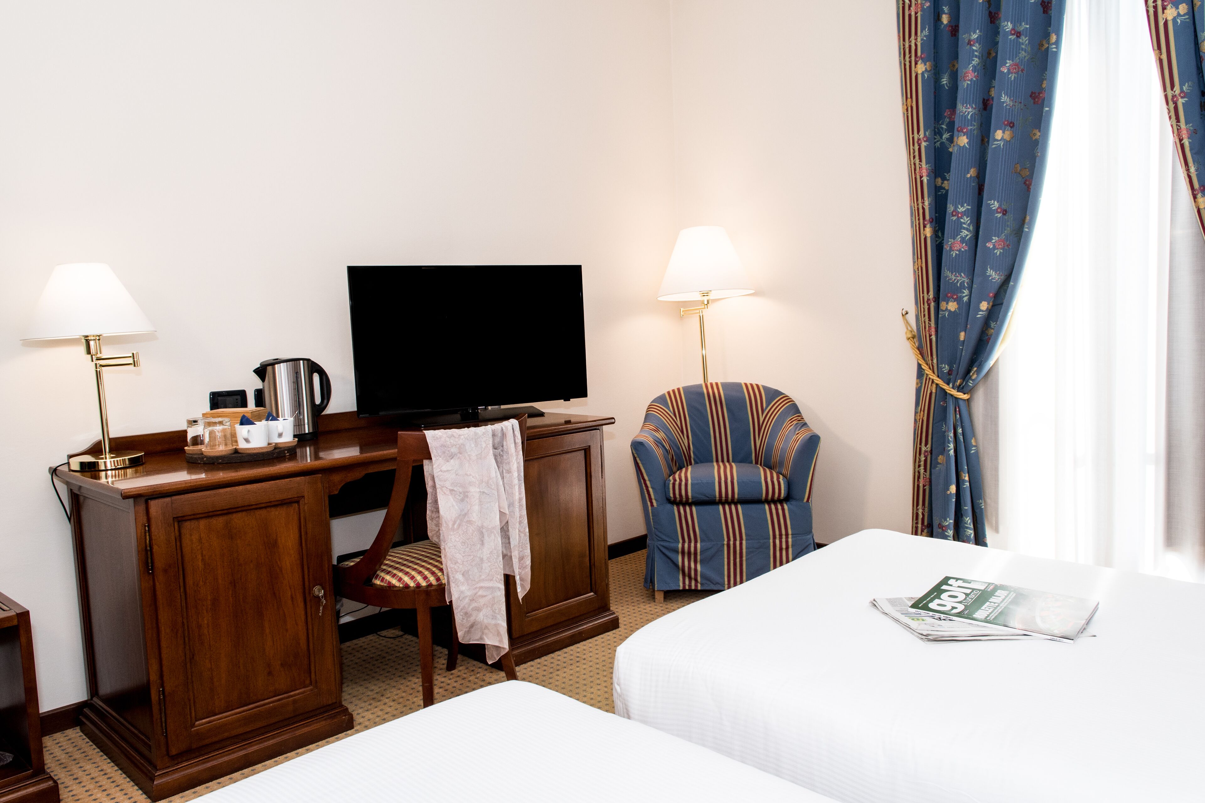 A hotel room with a bed, a desk with a television, a chair, and a lamp.
