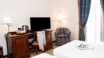 A hotel room with a bed, a desk with a television, a chair, and a lamp.