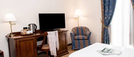 A hotel room with a bed, a desk with a television, a chair, and a lamp.
