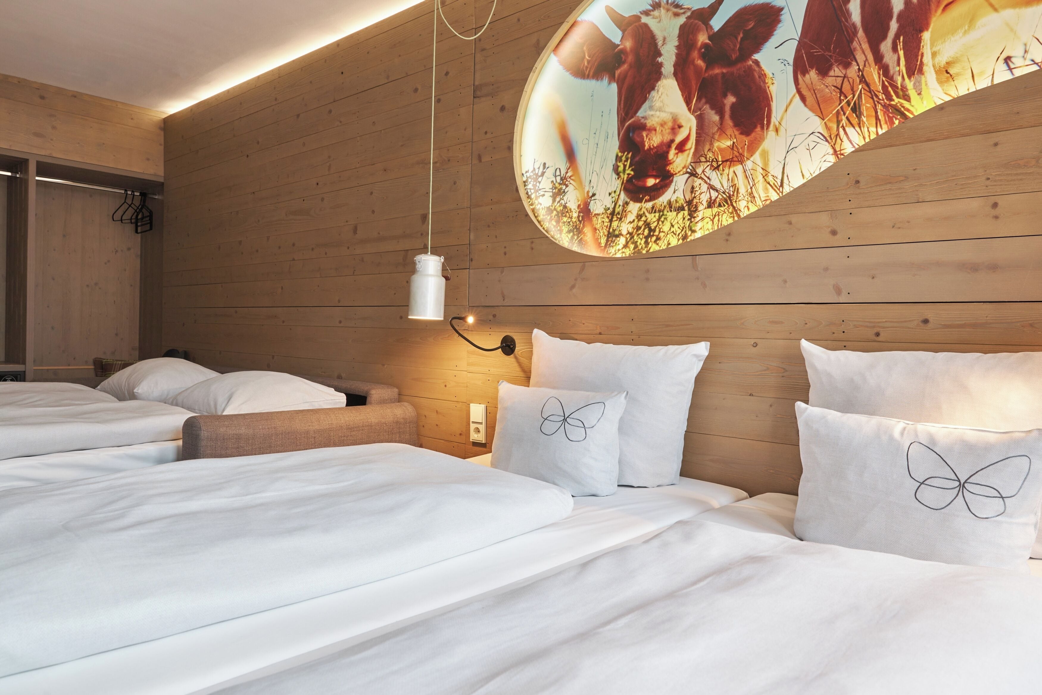 A bedroom with wooden walls, a bed with white bedding, and a unique cow-themed wall decoration.