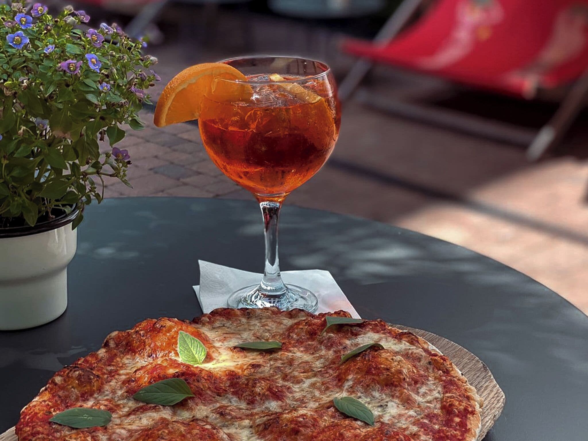 A table with a pizza and a glass of a beverage with an orange slice.