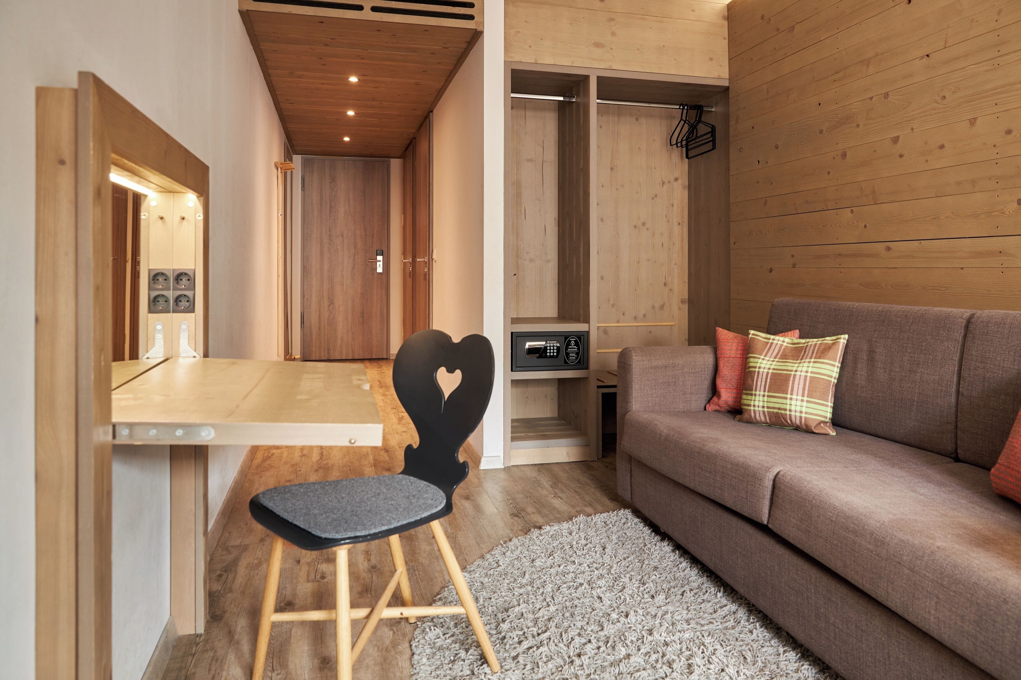 A modern interior with a wooden dining table, a black chair with a heart design, a brown sofa with plaid pillows, and a gray shag rug.
