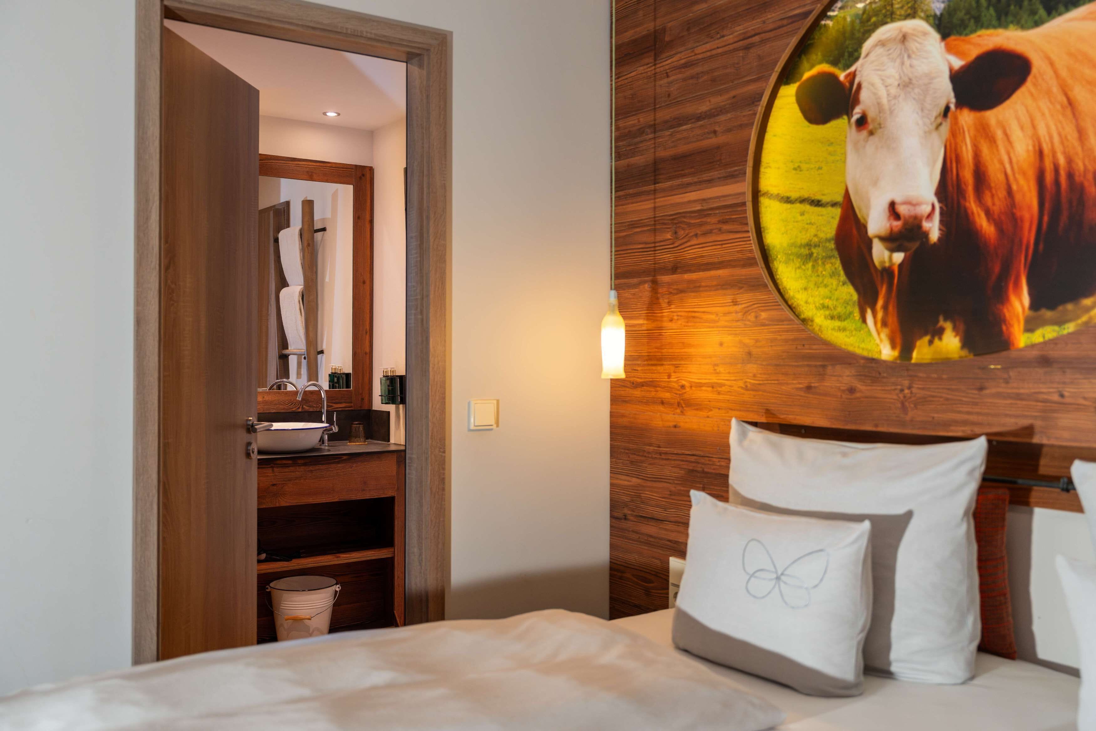 A hotel room with a wooden headboard, a bed with white bedding, a nightstand with a lamp, and a wall-mounted circular picture of a cow.