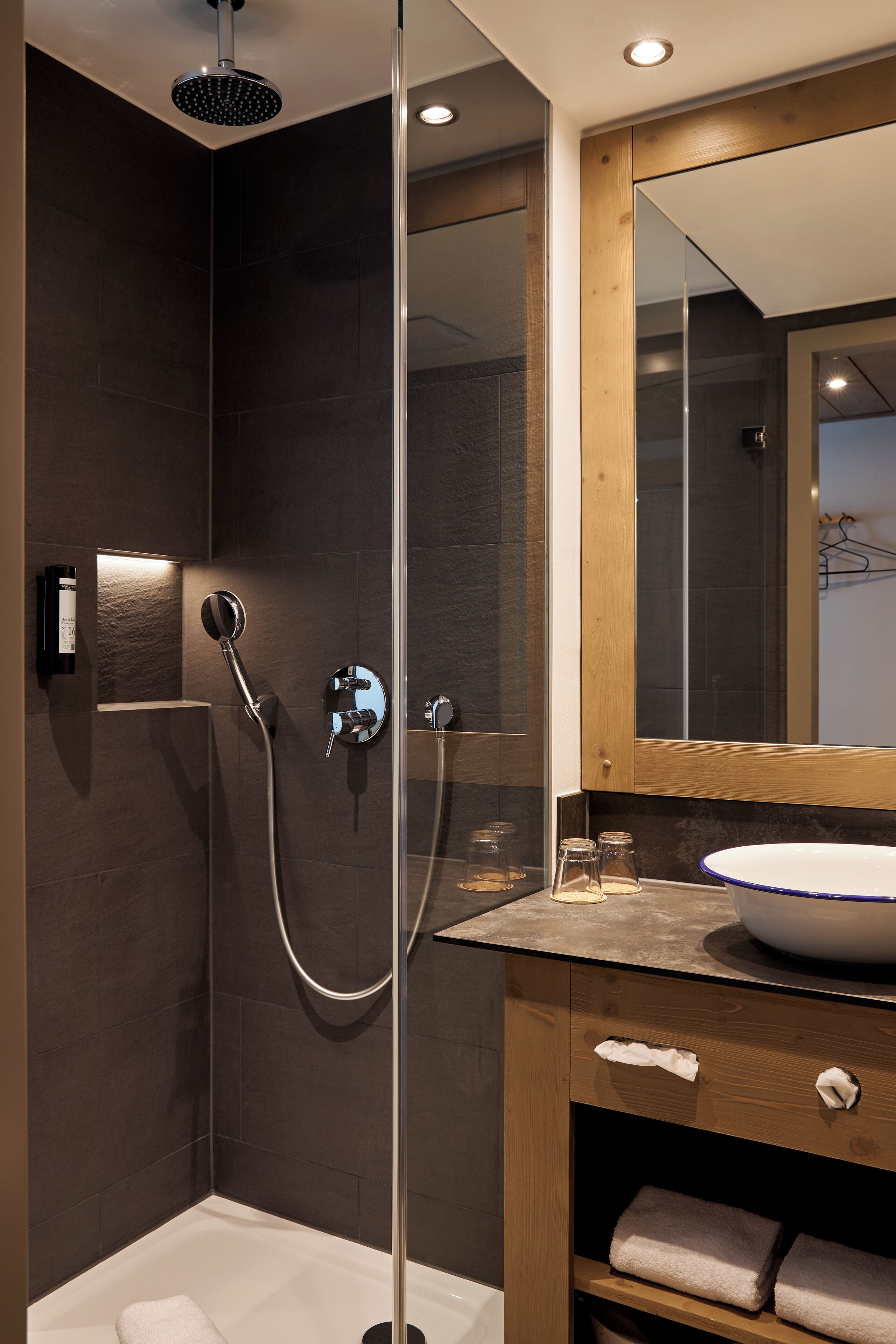 A modern bathroom with a glass-enclosed shower, a wooden vanity with a white sink, and a large mirror above the vanity.