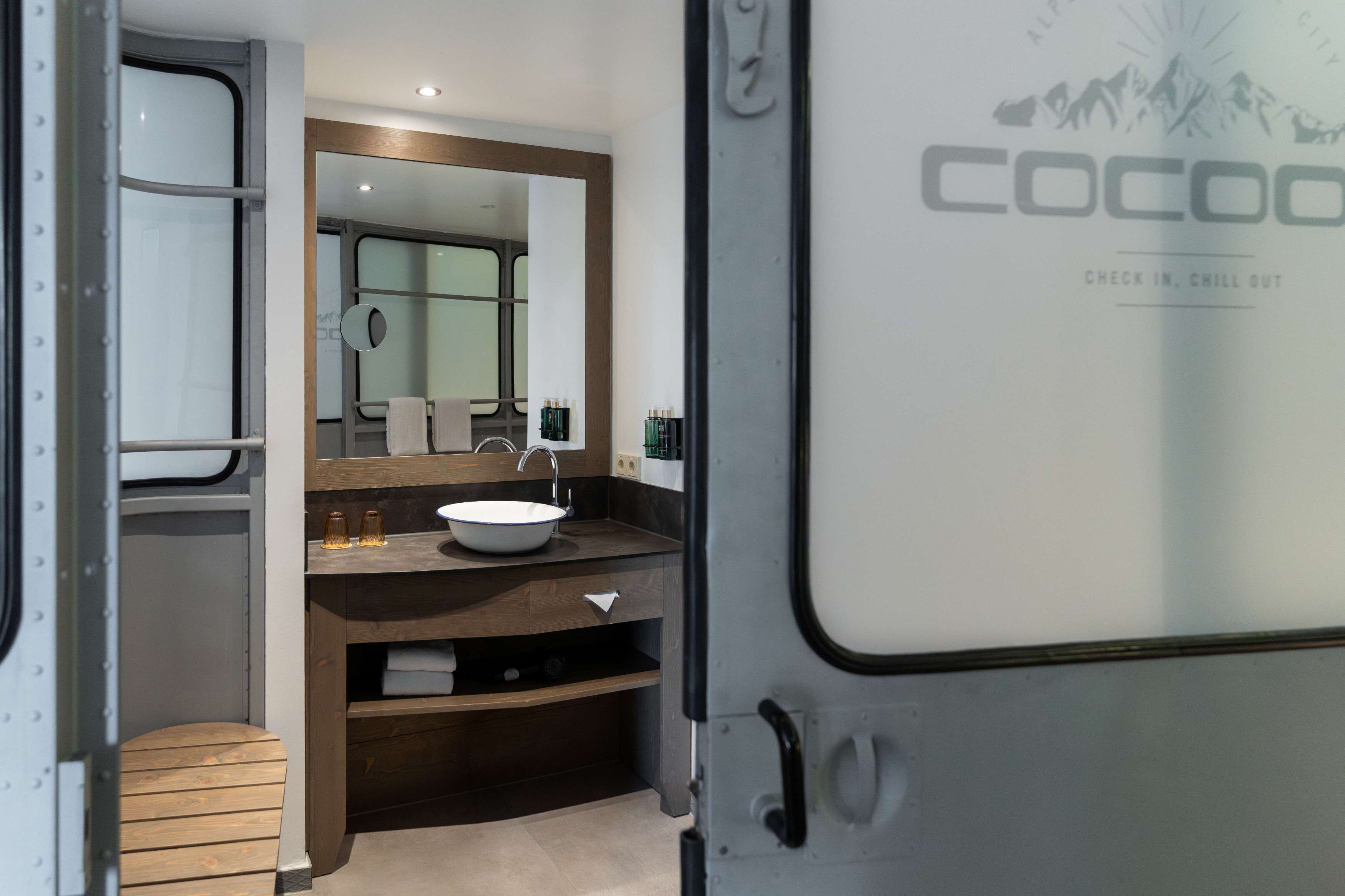 A compact, modern bathroom with a built-in sink, mirror, and storage drawers.