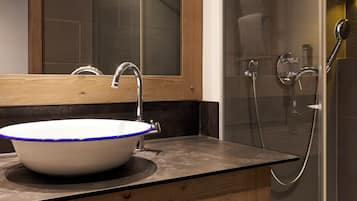 Ein modernes Badezimmer mit einem großen Spiegel, einem weißen Waschbecken mit blauen Akzenten, einer Holz-Kommode und einer Duschkabine aus Glas.