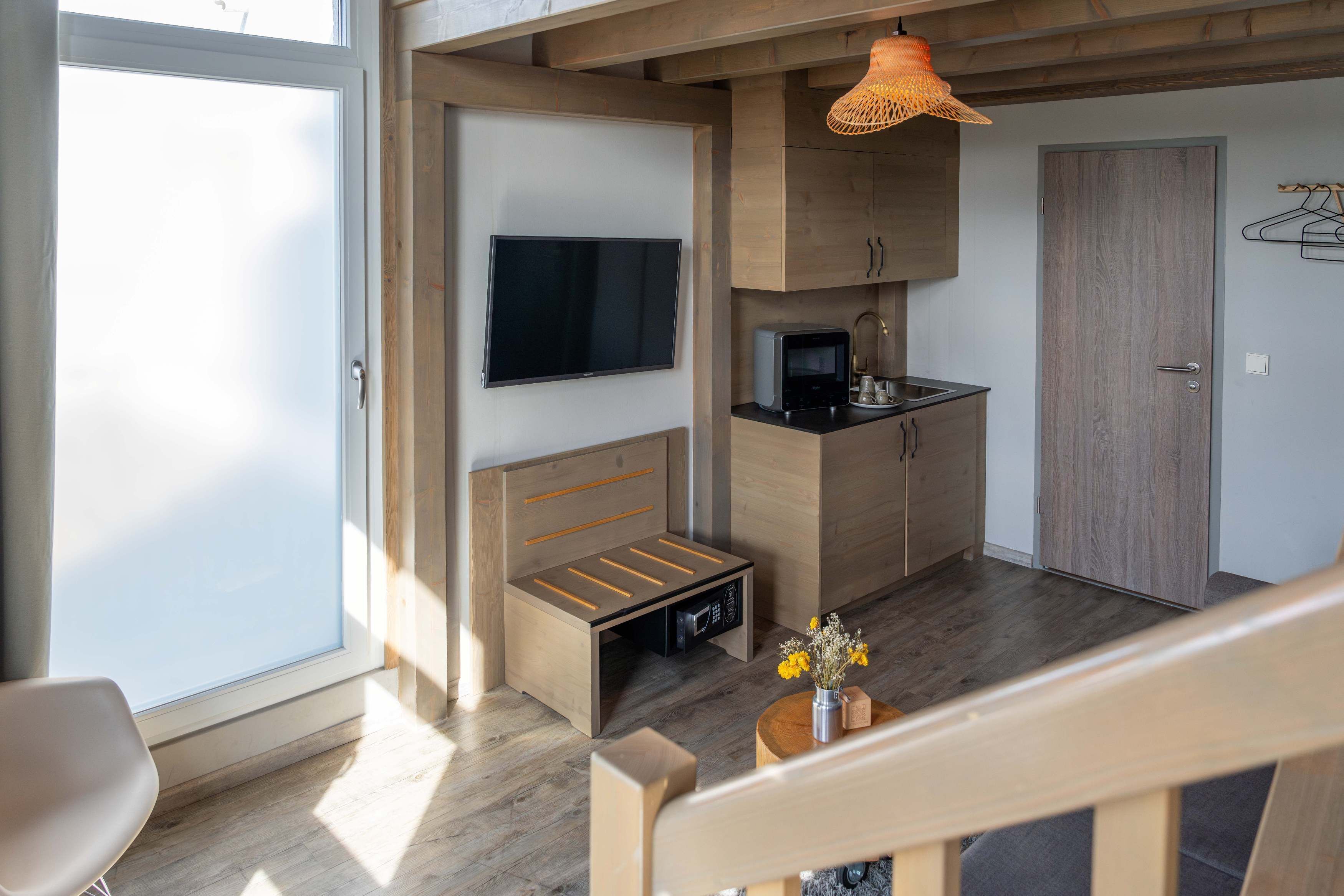Ein gemütlicher Raum mit Bett, Fernseher, Mikrowelle und einer kleinen Küchenzeile.