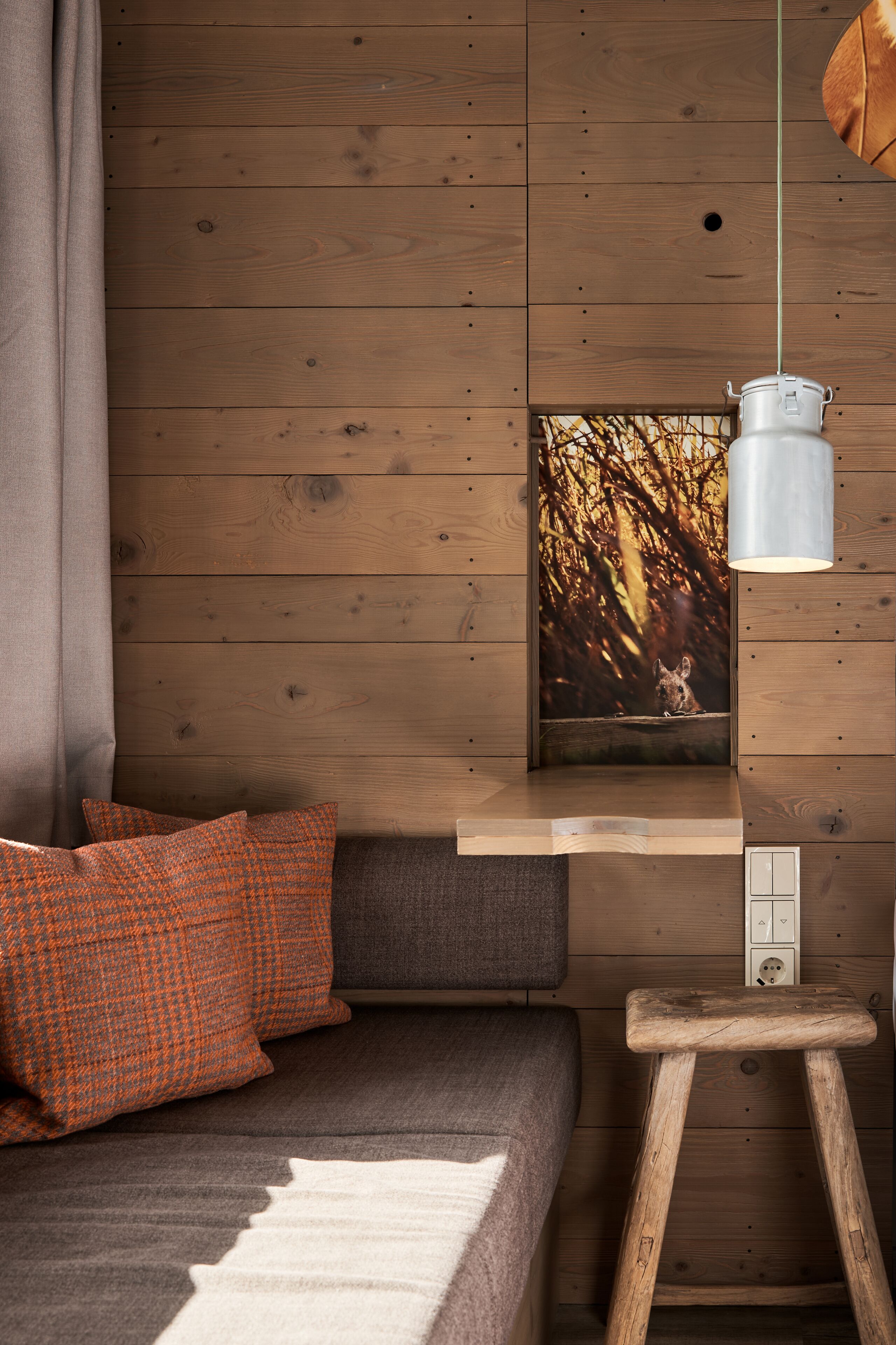 Een gezellige kamer met een houten wand, een grijze bank, kussens met oranje dessin, een witte lamp en een lijst met een foto van een hond.