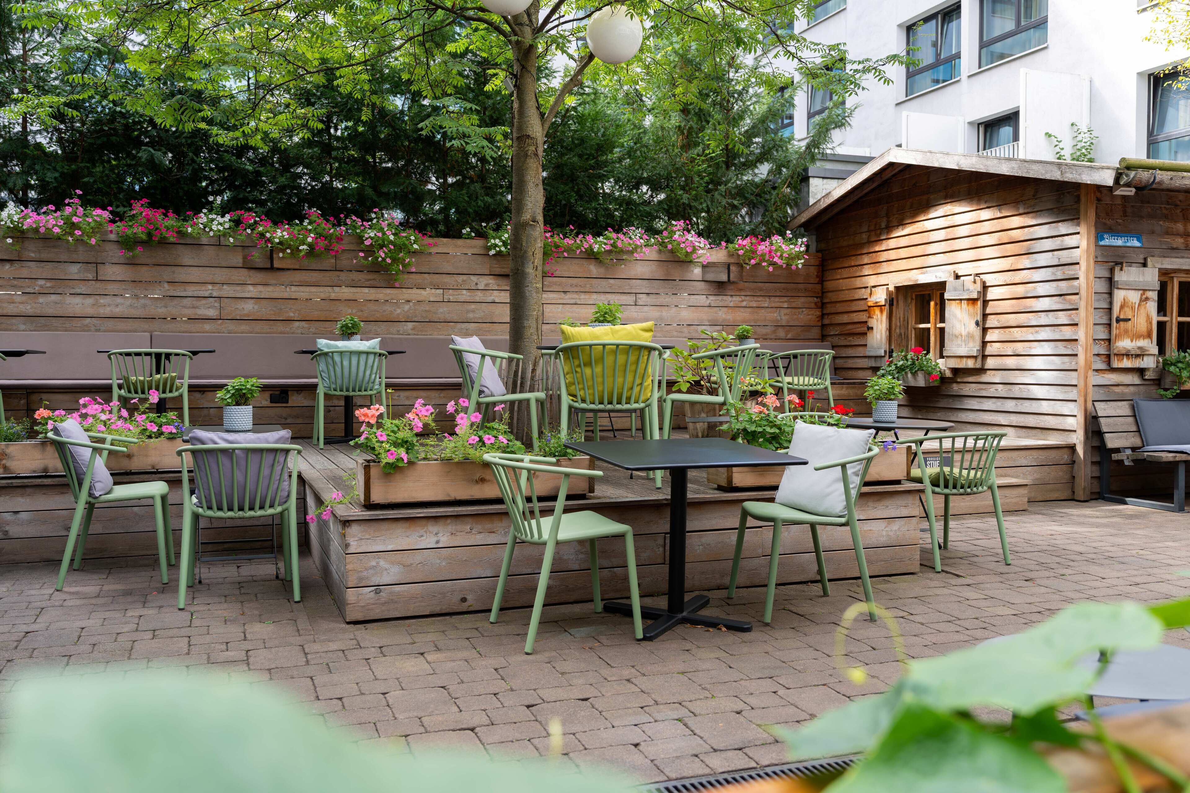Une terrasse extérieure avec des chaises et des tables en métal vert, entourée de jardinières en bois ornées de fleurs.