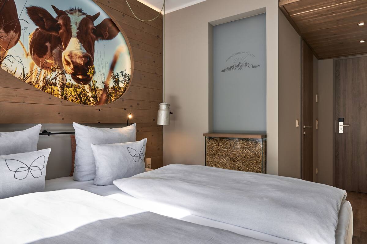 A bedroom with a wooden headboard, white bedding, and a wall-mounted artwork of cows.