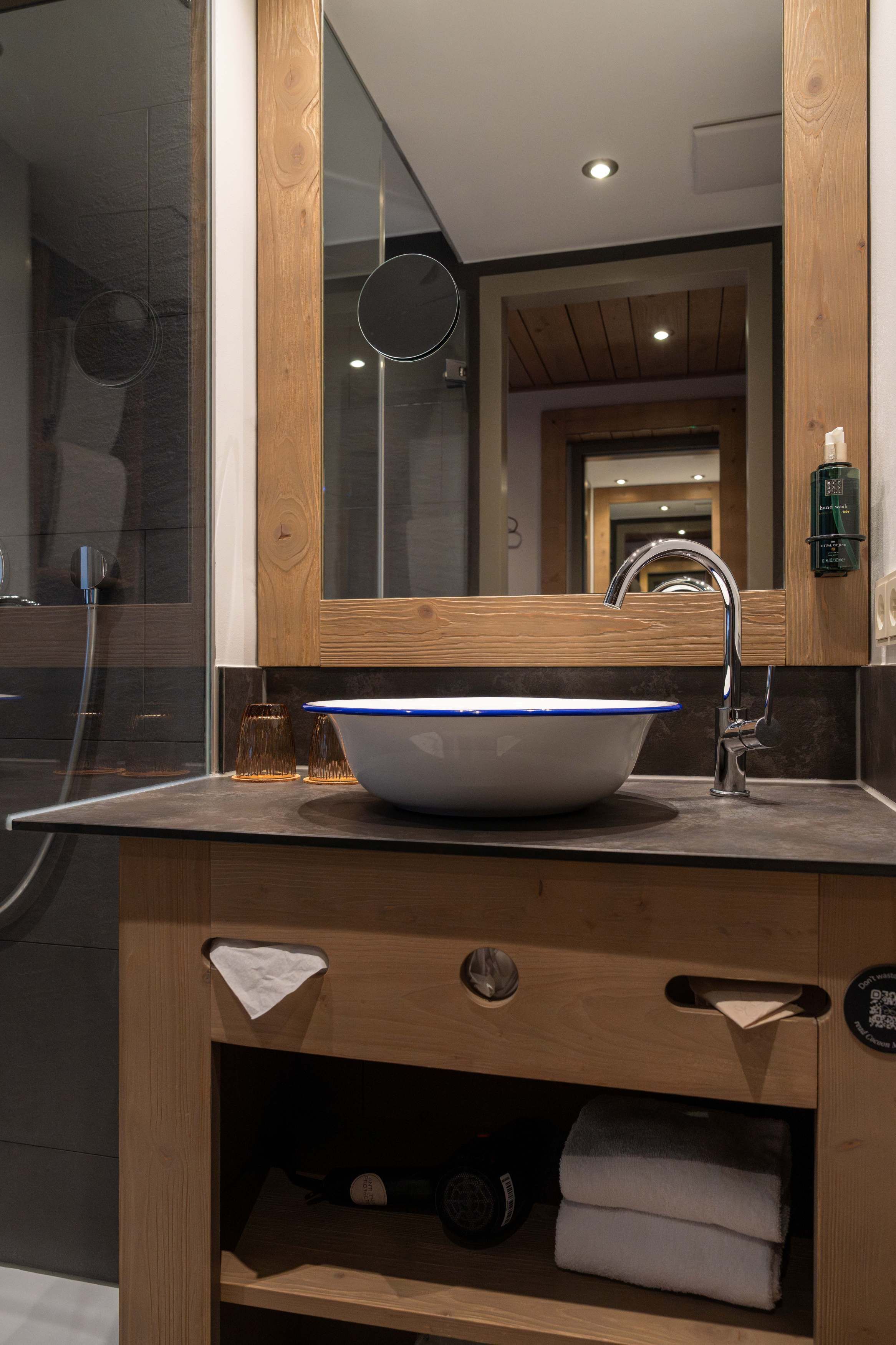 Een moderne badkamer met een grote spiegel, een houten wastafelmeubel en een waskom.