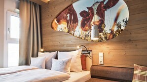 A hotel room with a bed, a sofa, and a wall-mounted TV displaying a nature scene. - Cocoon München Hauptbahnhof (Munich)