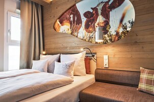 Habitación de hotel con cama, sofá y televisor de pared mostrando una escena natural.