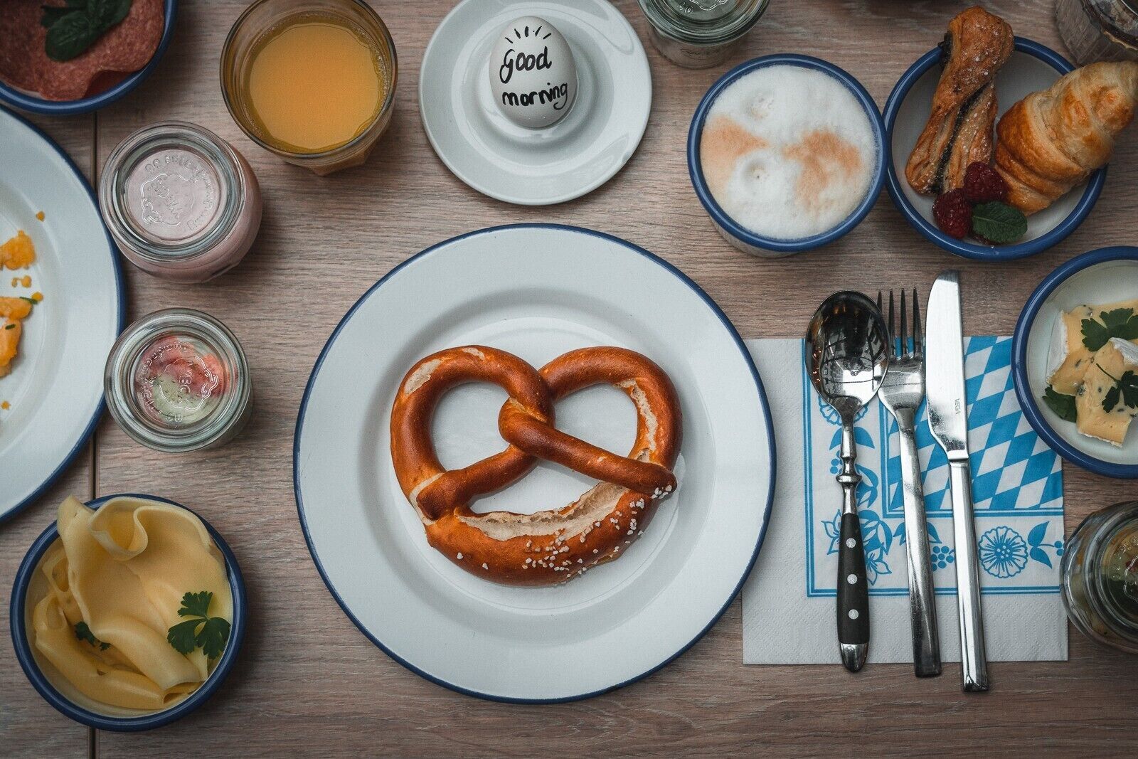 A breakfast setting with a pretzel, croissants, and various dishes on a wooden table.