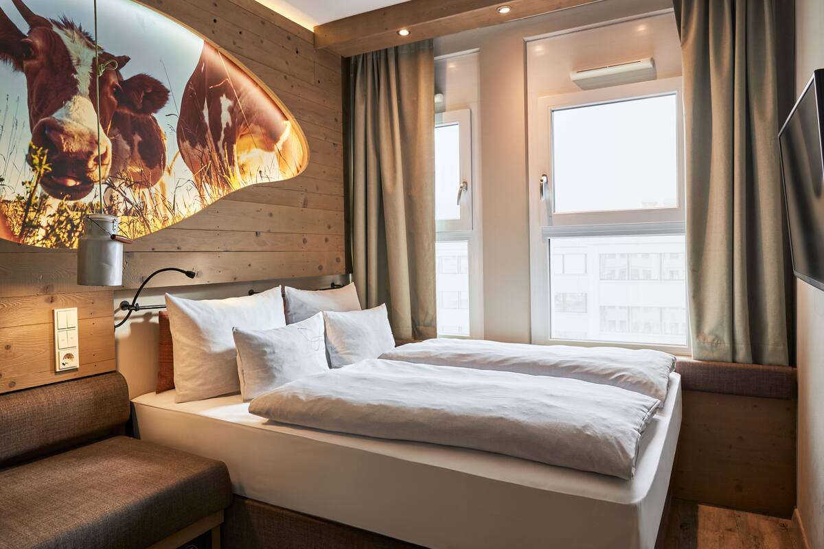 A modern hotel room with a large bed, a sofa, a flat-screen TV, and a wall-mounted artwork of cows.