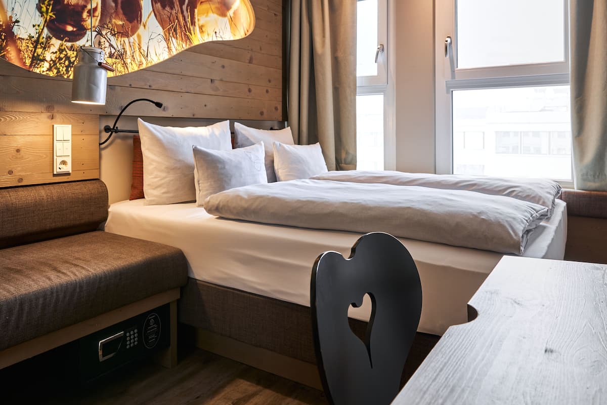 A bedroom with a bed, a bench, a table, and a wall-mounted lamp.