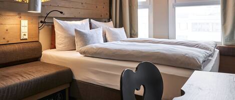 Un dormitorio con cama, una banca, una mesa y una lámpara de pared.