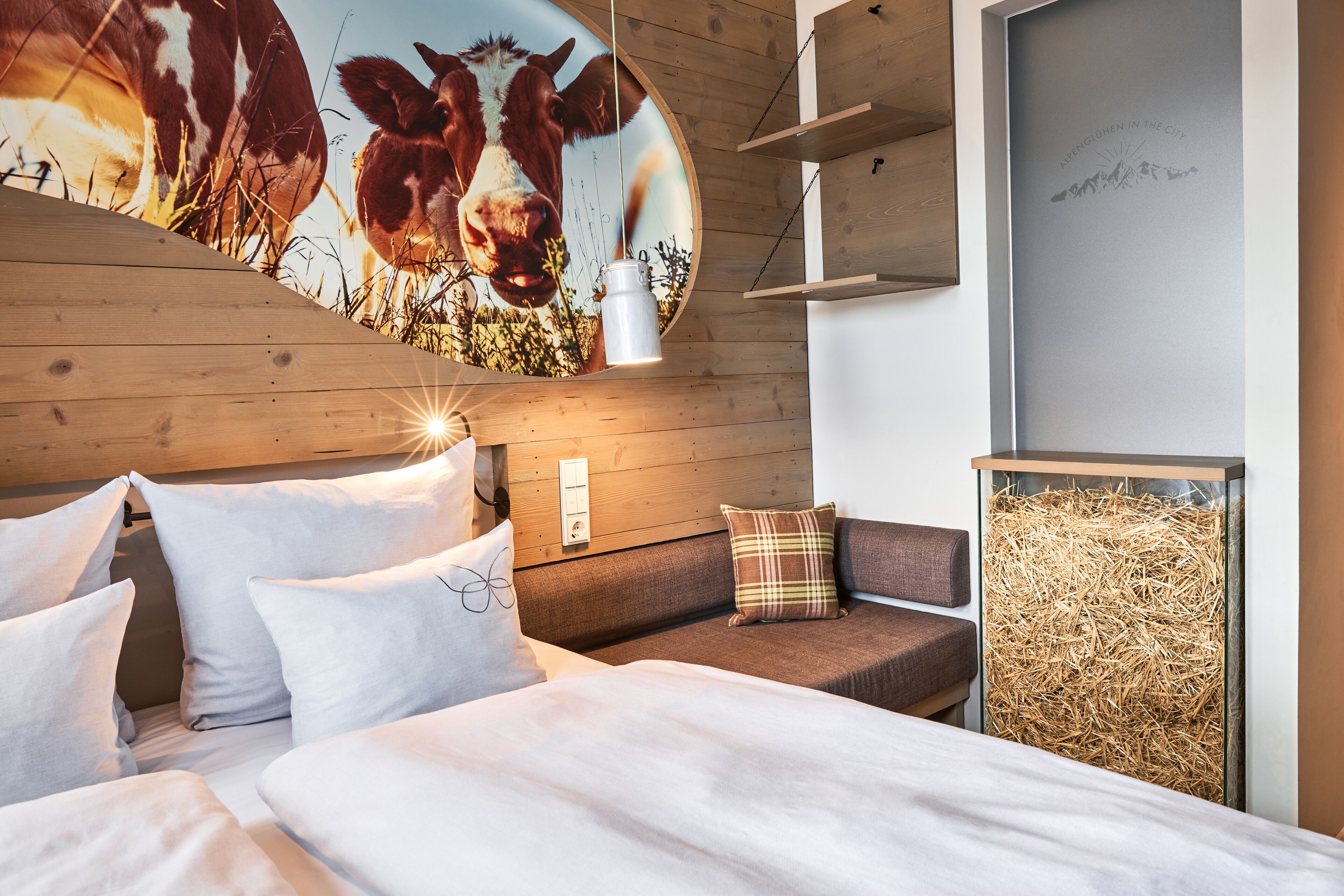 Een slaapkamer met een bed, kussens, een hoofdbord, een wandlamp, een bank en een kunstwerk aan de muur.