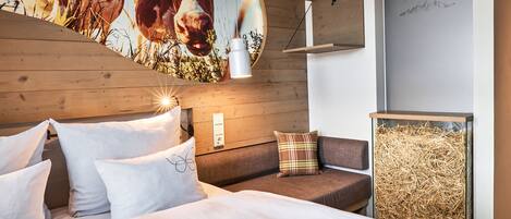 A bedroom with a bed, pillows, a headboard, a wall-mounted light, a sofa, and a wall art piece.