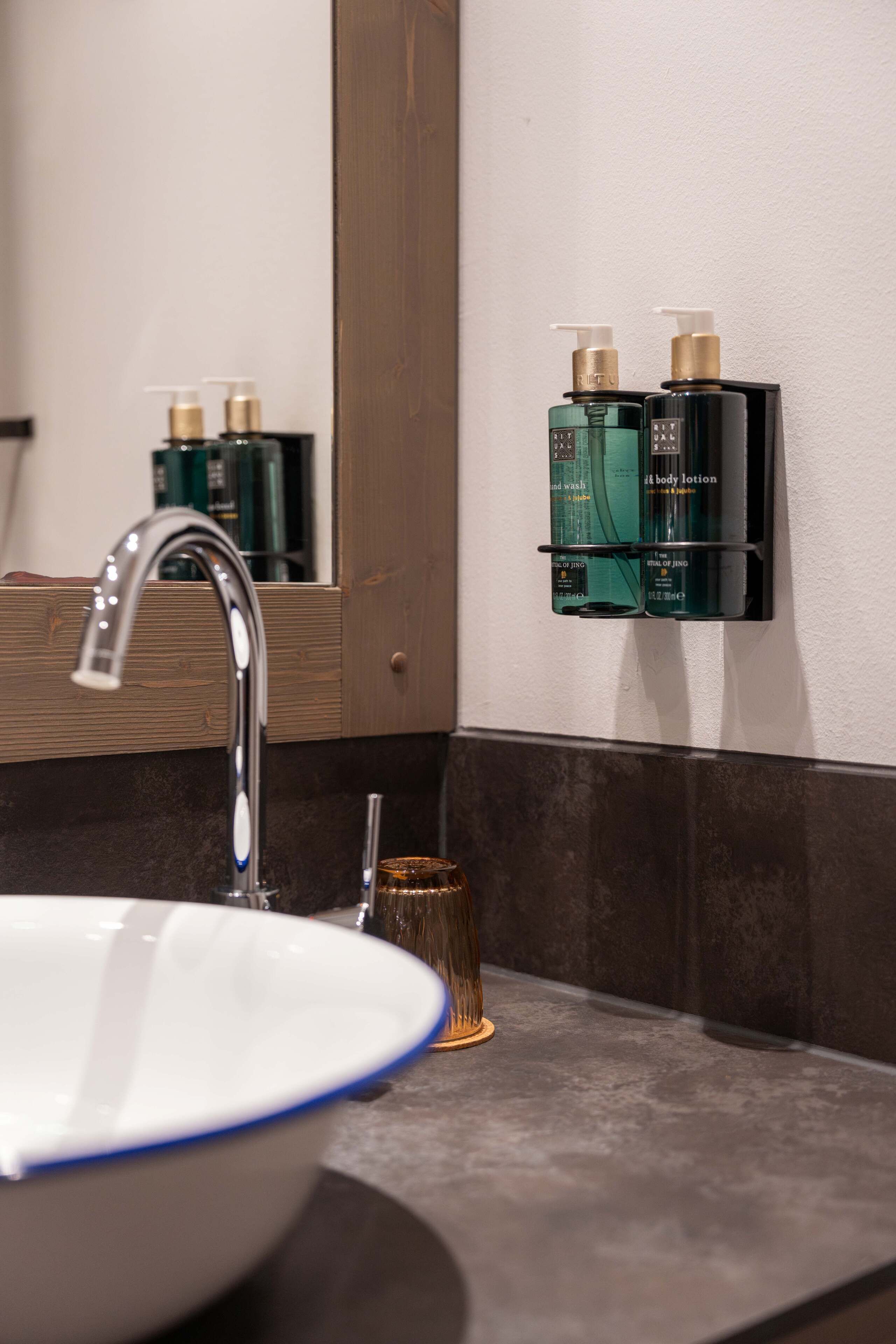 A bathroom with a modern sink, a mirror, and two bottles of lotion on a wall-mounted shelf.