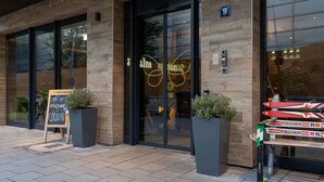 A modern building with large glass doors, a signboard, and outdoor seating. - Cocoon München Hauptbahnhof (Munich)