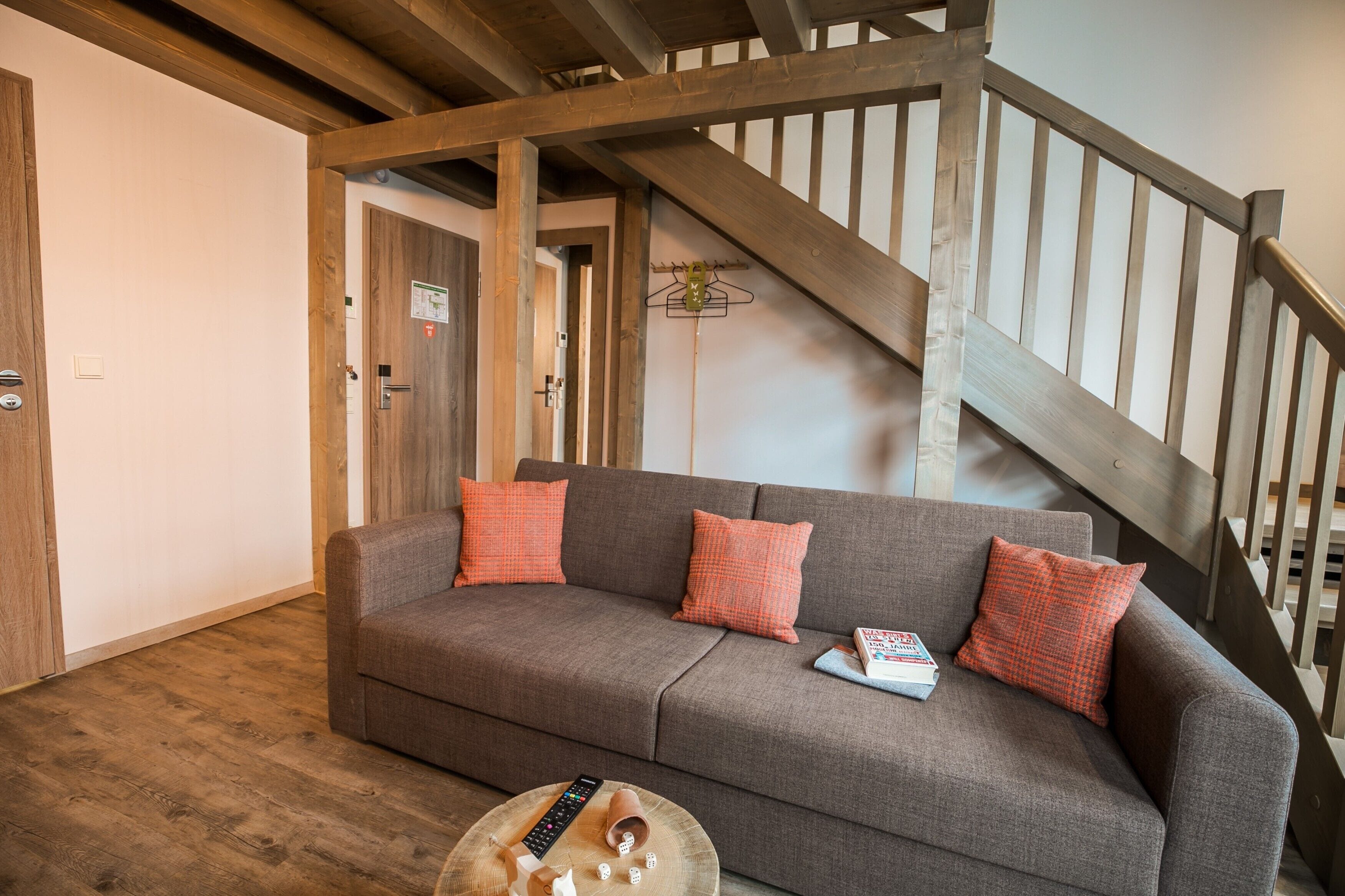 A living room with a grey sofa, wooden beams, and a staircase.