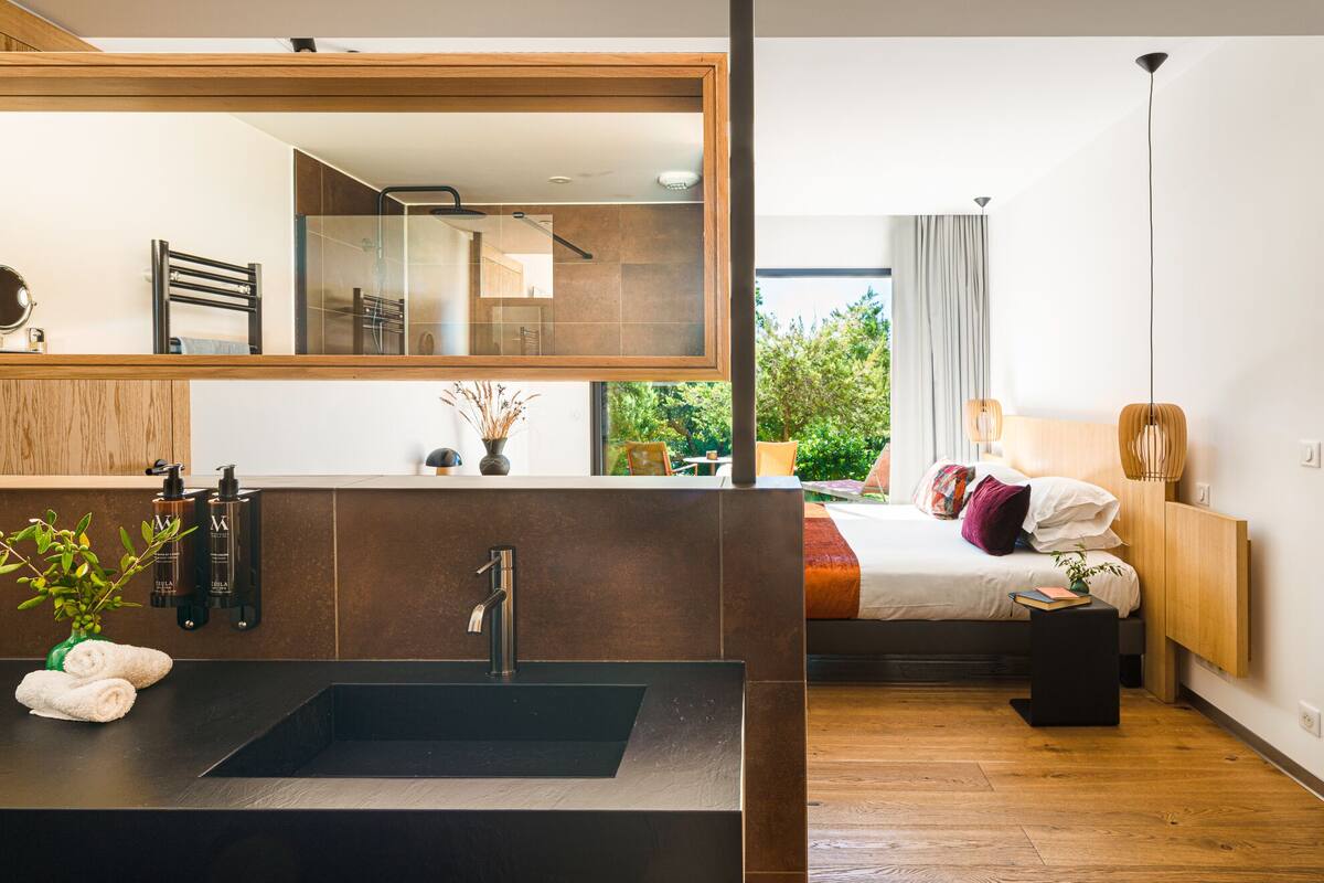 Une salle de bain moderne avec un grand miroir, un lavabo noir et un espace douche.