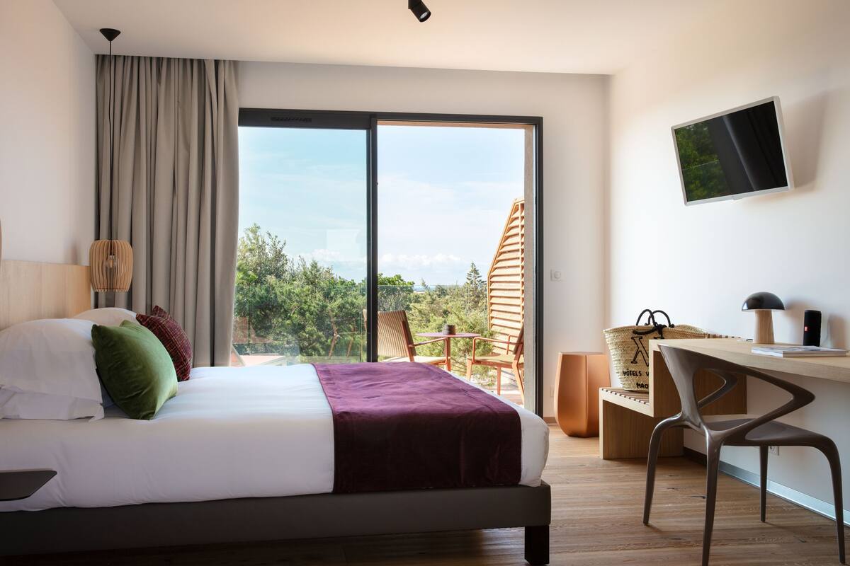 Une chambre d’hôtel équipée d’un lit, d’un bureau, d’une chaise, d’une télévision et offrant une vue sur la verdure environnante.