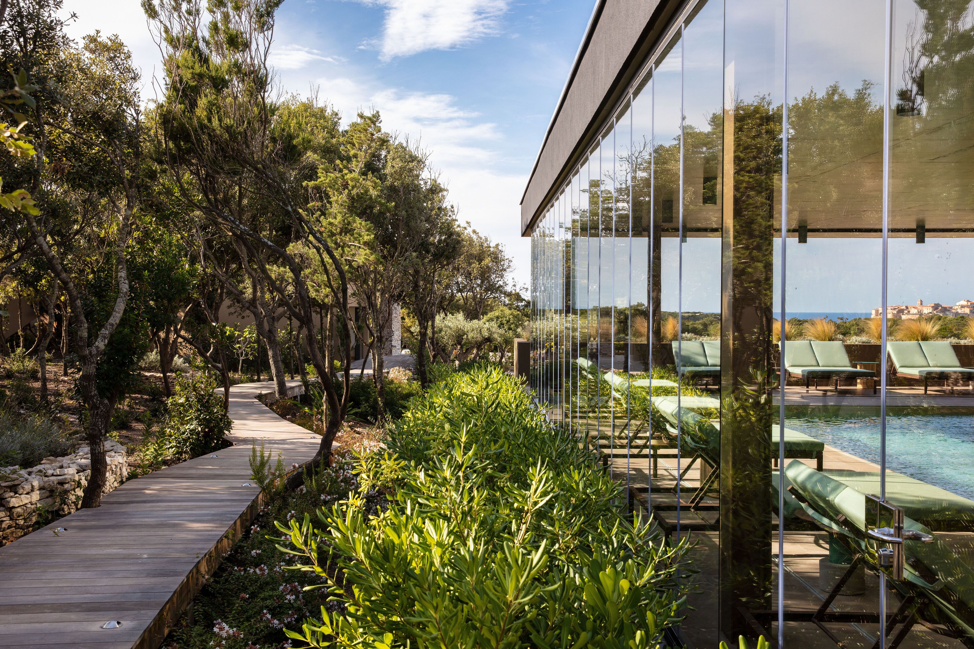 A poolside area with lounge chairs, a wooden pathway, and lush greenery.