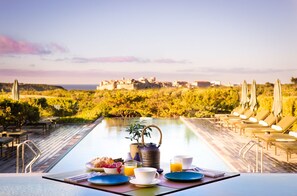 A breakfast table with plates, cups, and a teapot, overlooking a pool and a villa. - Hôtel et SPA Version Maquis Citadelle (Bonifacio)