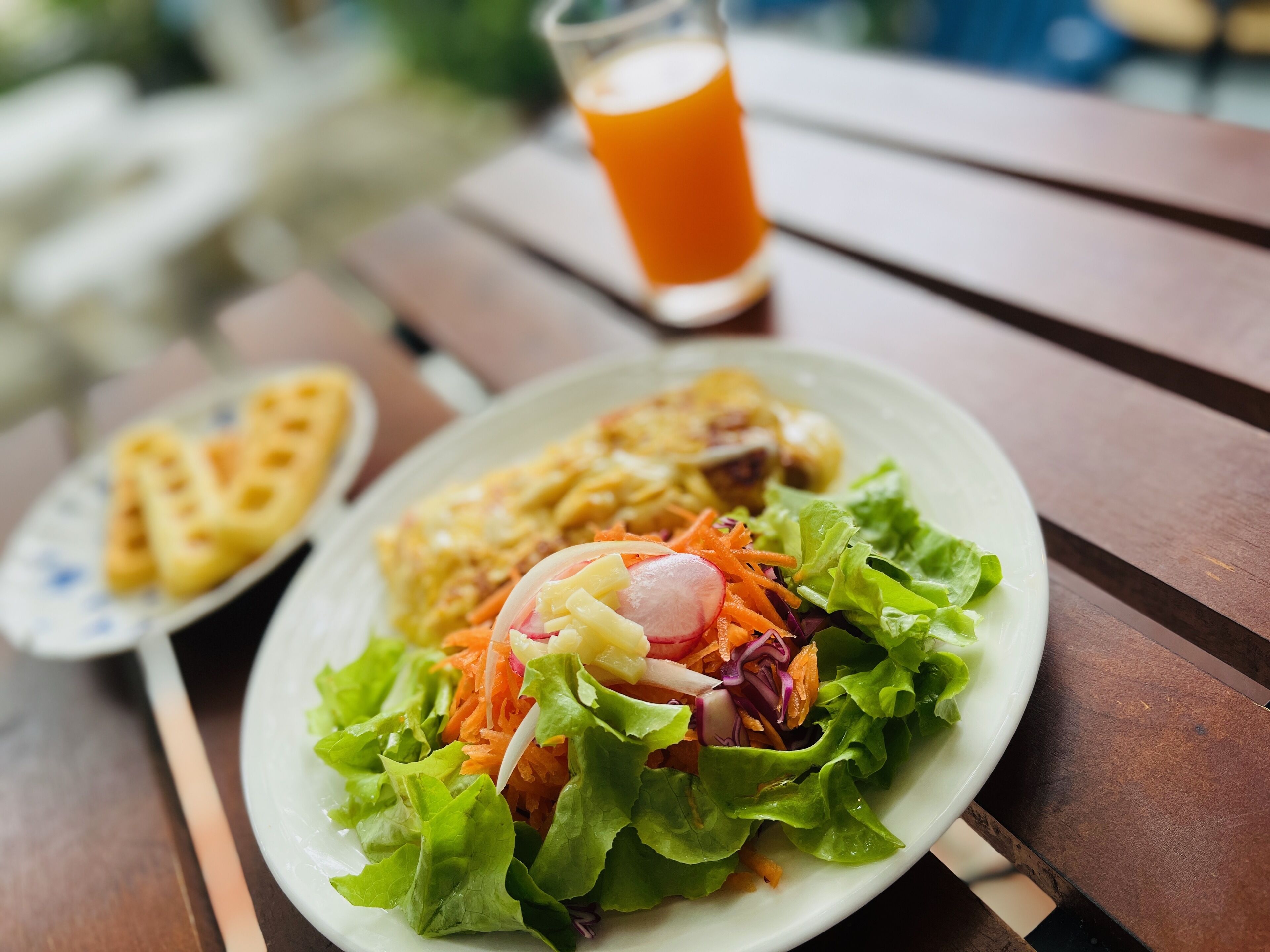 A meal on a wooden table with a salad, a heart-shaped pastry, and a glass of orange juice.