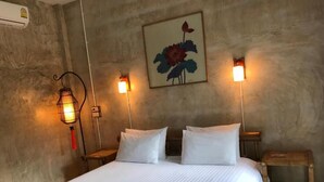 Una cama bien tendida con sábanas blancas, dos mesitas de noche, una lámpara de pared y una obra de arte floral enmarco.
