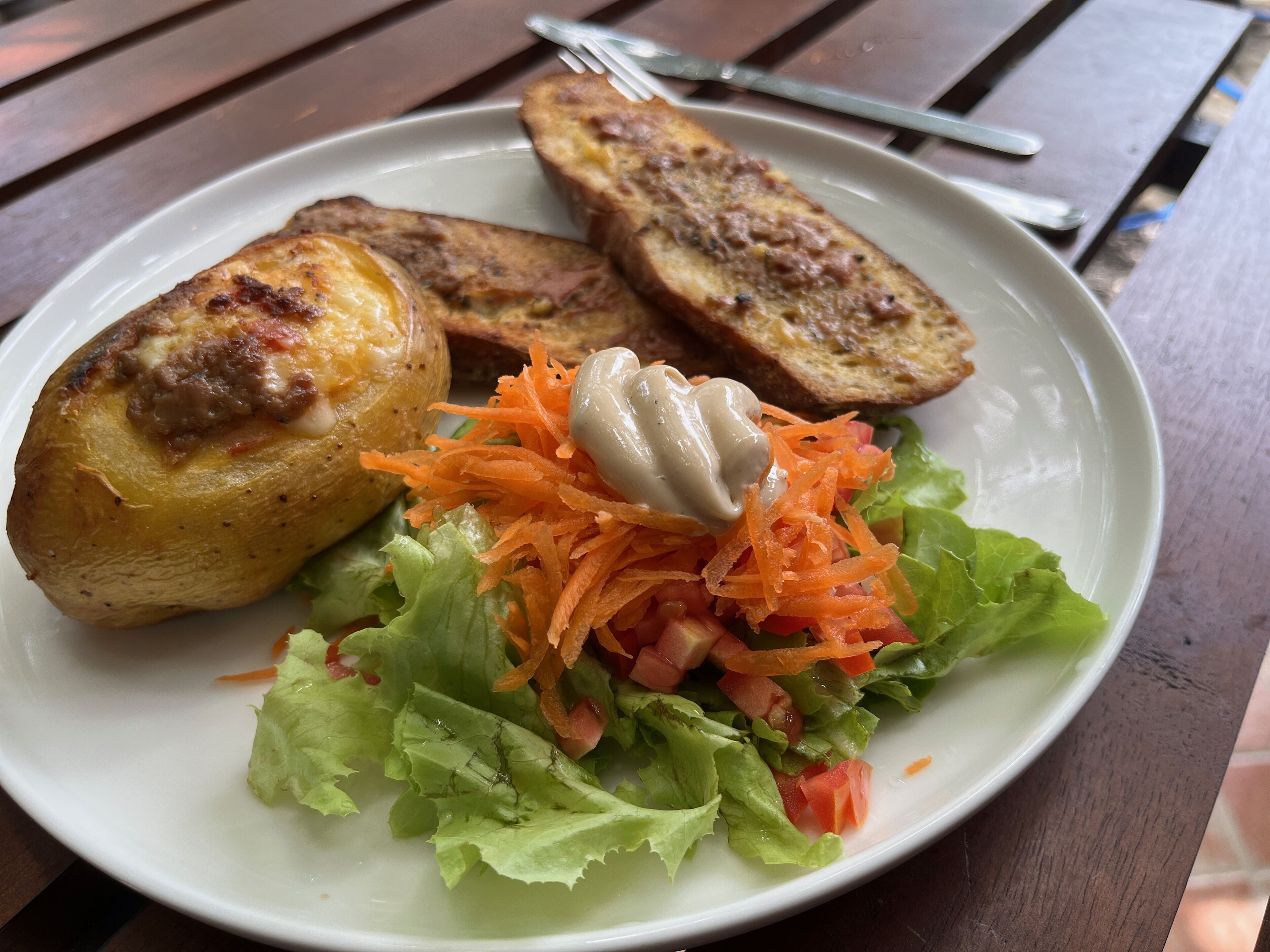 Une assiette avec une salade, deux tranches de pain grillé et un morceau de viande grillée.