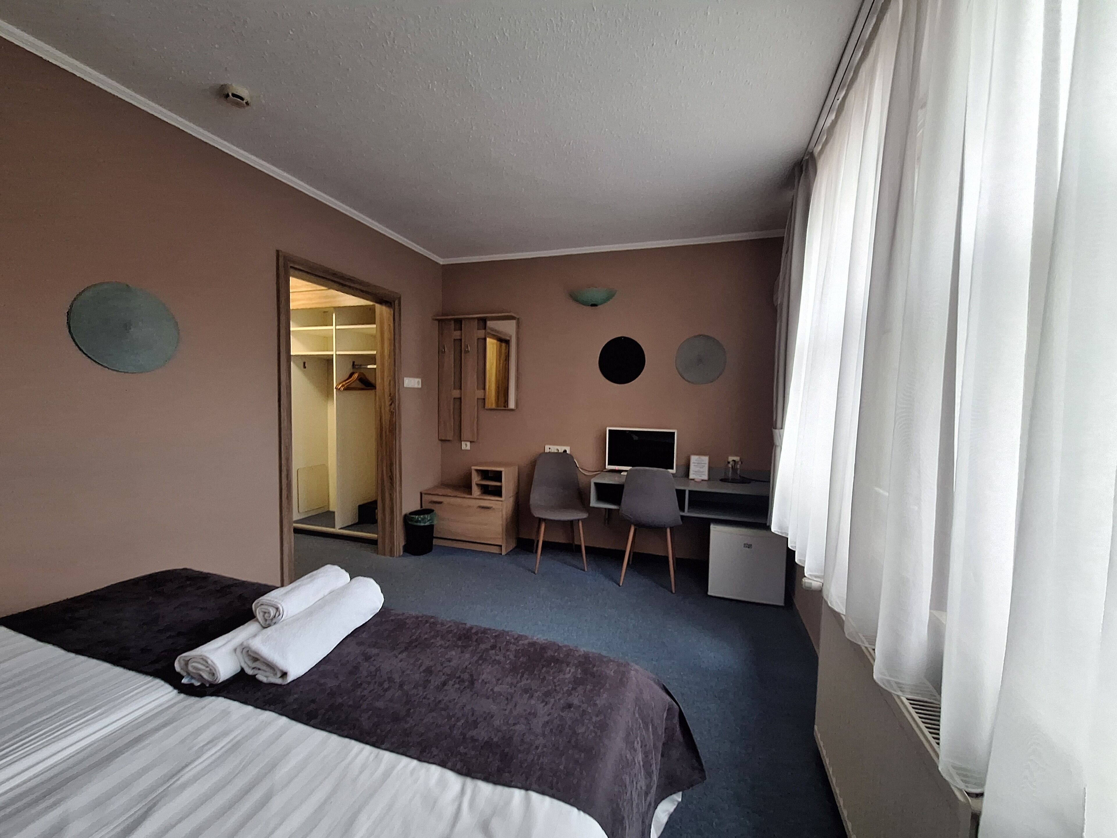 Una habitación de hotel con cama, escritorio, silla, computadora y armario.