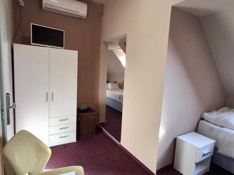 Quarto de hotel pequeno, com cama, uma mesinha, cadeira, guarda-roupa e espelho.