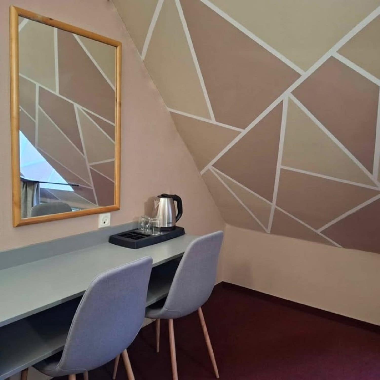 Ein Zimmer mit Schreibtisch, zwei Stühlen, einem Wasserkocher und einem Spiegel an der Wand.