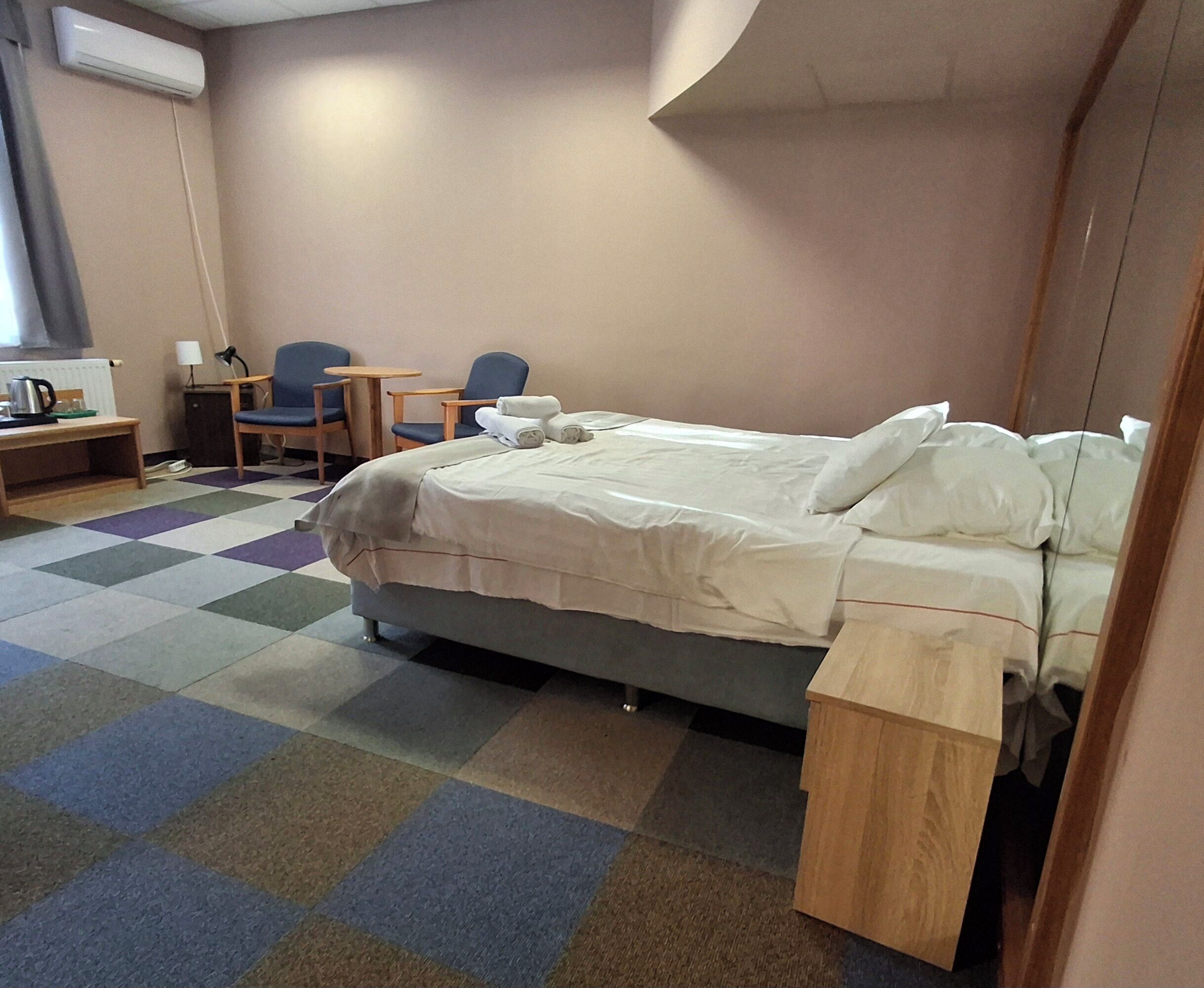 A hotel room with a bed, a desk, a chair, and a small table.