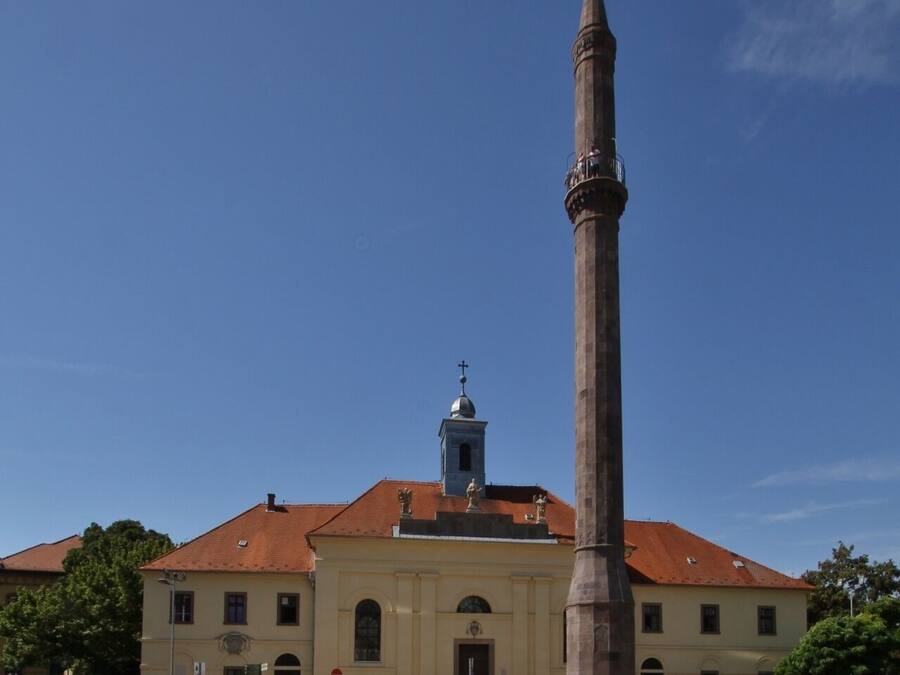 Una iglesia con un campanario alto y un gran obelisco al frente.